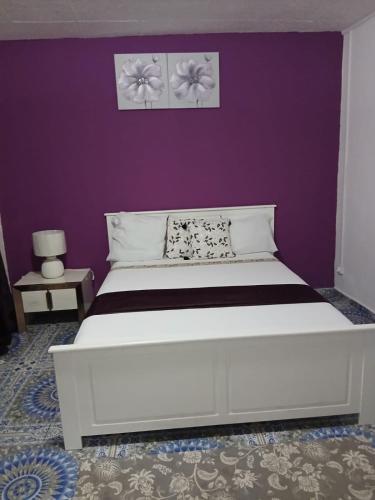 a bedroom with a white bed with a purple wall at Les Jasmins partagées in Mamoudzou