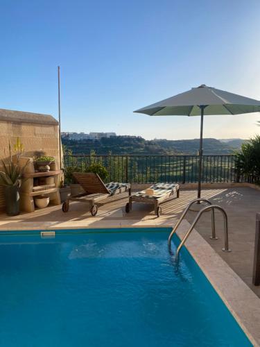 a swimming pool with an umbrella and a table and chairs at Ta’ Giljan B&B Gozo in Xagħra