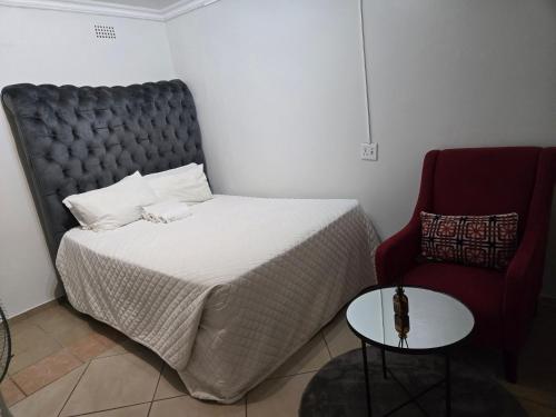 a bedroom with a bed and a red chair at Cjabaledi Guesthouse in Centurion