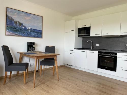 a kitchen with white cabinets and a wooden table with chairs at Ferienwohnung Watt n Deichblick in Friedrichskoog