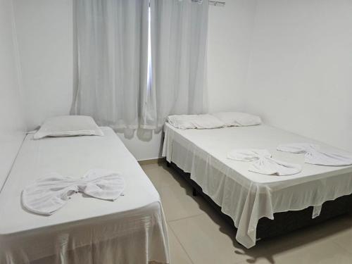 two beds in a room with white curtains at Apto Garden Taperapuan 2 quartos com suíte in Porto Seguro