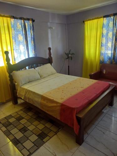 a bedroom with a bed with a wooden frame and yellow curtains at Sea View Guest Accommodation in Roseau