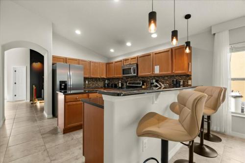 a kitchen with wooden cabinets and a bar with chairs at 5 Bedrooms 3 Bathrooms Veranda Palms 4458 NP in Orlando
