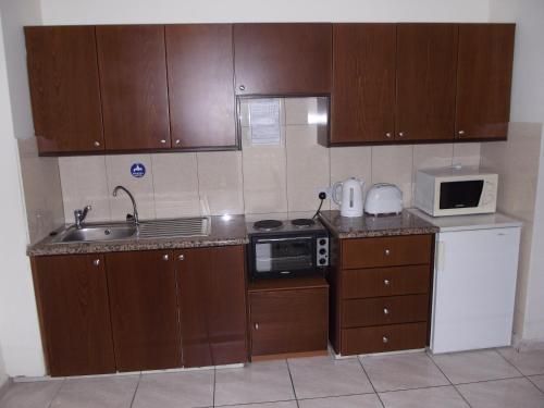 a kitchen with wooden cabinets and a sink and a microwave at Kefalonitis Hotel Apartments in Paphos City