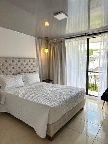 a bedroom with a white bed and a large window at Hotel Alamos del Bosque in Pereira