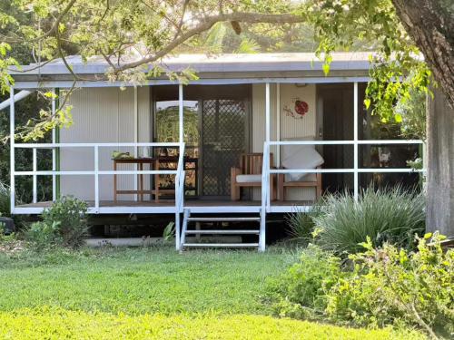 a white cottage with a porch and a chair at Feng Shui Sugarcane Cabin in Proserpine