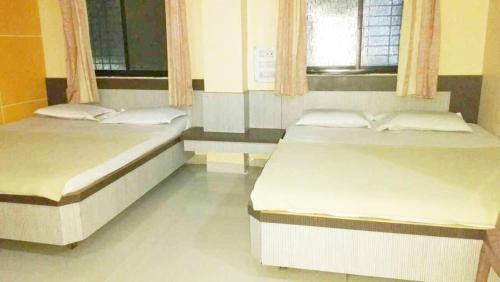 two beds in a room with two windows at Laxmi Guest House in Shirdi