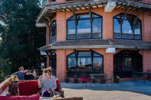 a woman sitting on a couch in front of a brick building at Peaceful Cottage & Cafe Du Mont in Nagarkot