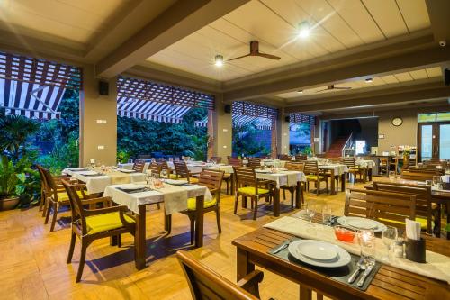 restauracja z białymi stołami, krzesłami i oknami w obiekcie Ayrest Hua Hin Hotel w mieście Hua Hin