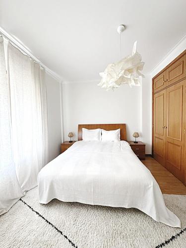 a white bedroom with a white bed and a chandelier at Casa da Maria - T1 perto da praia do Baleal com piscina in Ferrel
