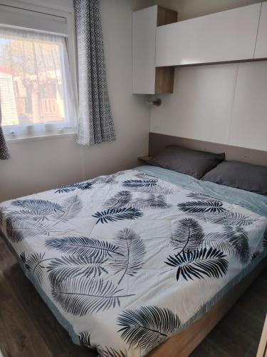 a bedroom with a bed with a black and white blanket at MOBIL-HOME "B30" tout confort avec piscine & lave-linge gratuit in Mimizan