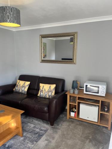 a living room with a leather couch and a mirror at Silvermead stables Own access studios near Plymouth Life Centre FREE parking in Plymouth