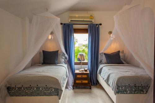 two beds in a bedroom with blue curtains and a window at Southern Lanta C9 in Ko Lanta