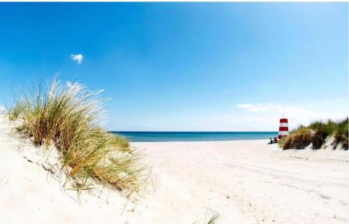 a beach with a red and white lighthouse and the ocean at Lækkert sommerhus i gåafstand til by og strand in Bøtø By