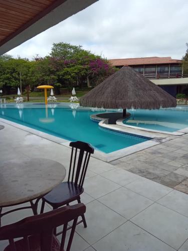 a pool with a table and a straw umbrella at Flat studio monte castelo gravatá PE in Bezerros