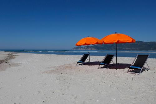 three chairs and two umbrellas on a beach at Hotel Casa Palmela - Small Luxury Hotels of The World, Hotel & Villas in Setúbal
