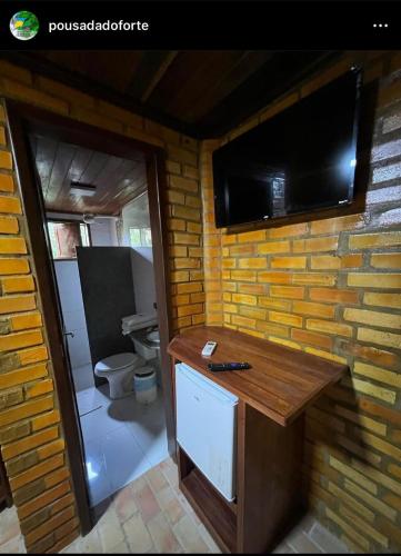 a bathroom with a toilet and a television on a brick wall at Pousada do Forte in Barra do Cunhau