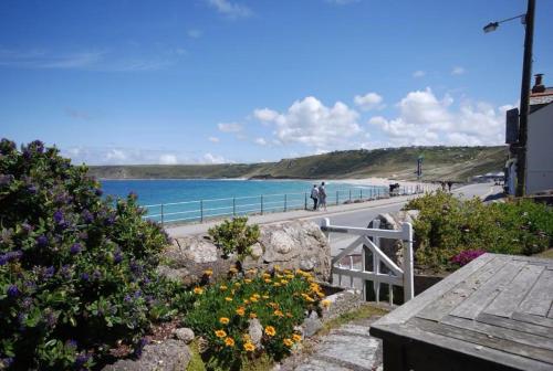 a view of a beach with a bench and flowers at Riviera Low Tide in Sennen Cove