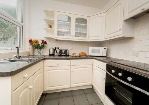 a white kitchen with white cabinets and a sink at Riviera Low Tide in Sennen Cove
