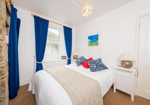 a bedroom with a bed with blue curtains and a window at Riviera Low Tide in Sennen Cove