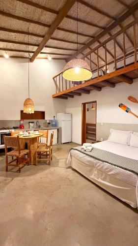 a bedroom with a bed and a table and a kitchen at Vila Alta Caraíva in Caraíva