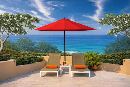 a patio with two chairs and a red umbrella at Pacific Club Resort in Karon Beach