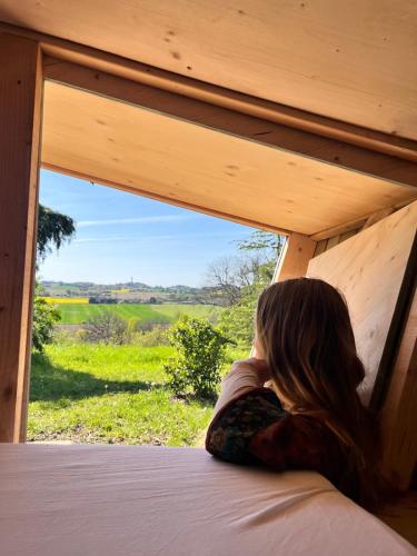 a woman laying on a bed looking out a window at Cabane étape in Idrac-Respailles