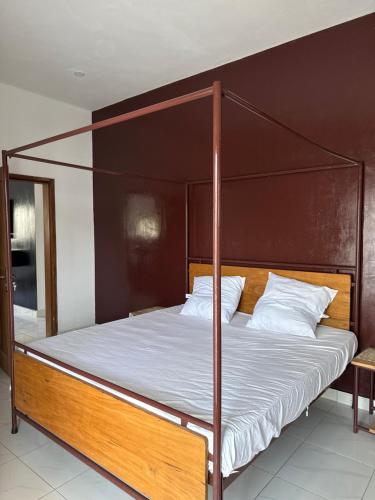 a bed with a wooden frame and white sheets at Chez Sira in Warang