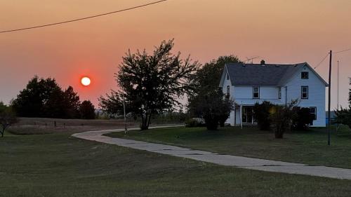 a white house with the sunset in the background at Sunset View Centennial Farm in Mancelona