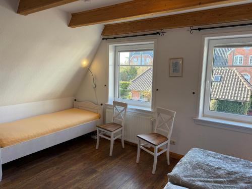 a bedroom with two chairs and a bed and two windows at Sütjers Hüs in Norddorf
