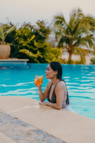 a woman sitting next to a swimming pool eating a piece of food at Casa Ceiba Huatulco - Adults Only in Santa Cruz Huatulco