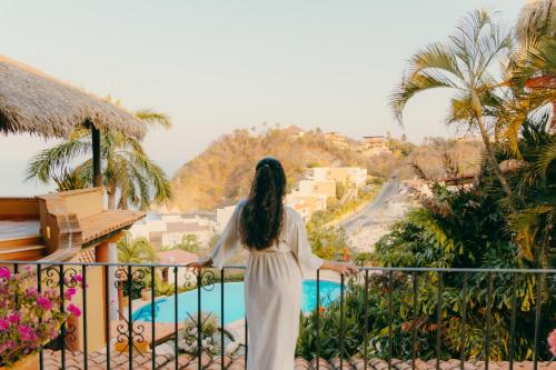 a woman in a white dress standing on a balcony overlooking a pool at Casa Ceiba Huatulco - Adults Only in Santa Cruz Huatulco