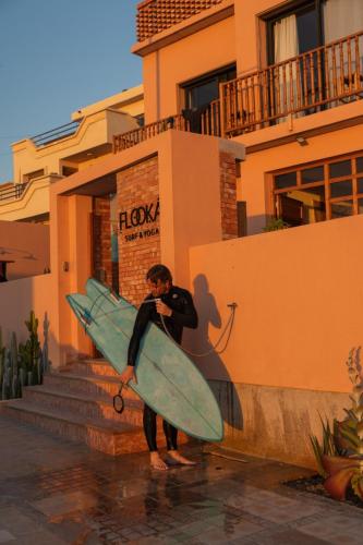 a man holding a surfboard in front of a building at Flooka Surf Yoga in Imsouane