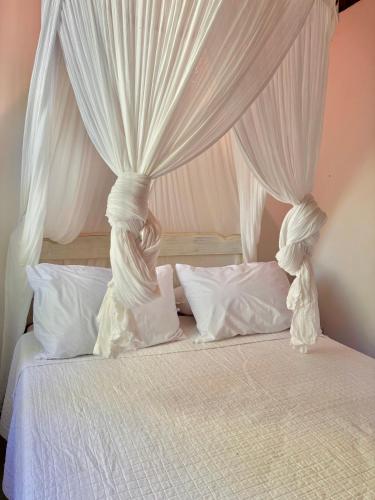 a white canopy bed with white curtains and pillows at Casa Botanique Jungle Retreat in Abraão