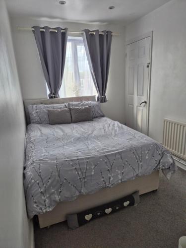 a bedroom with a bed with gray comforter and a window at 5 min from airport, luxury 2 bed apartment in Luton