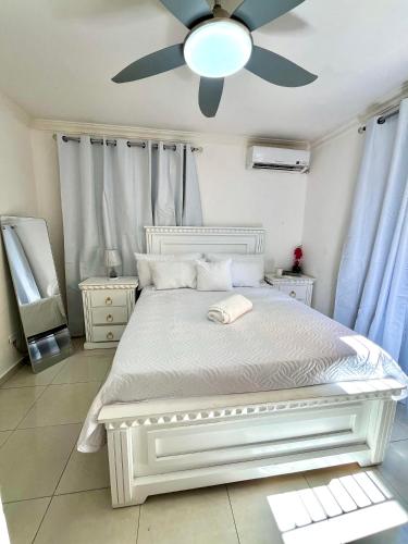 a bedroom with a white bed with a ceiling fan at Moderno Apartment Near the Ocean Santo Domingo Este Wife ,AC in La Francia