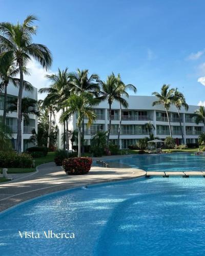 a swimming pool in front of a building with palm trees at Lujoso Departamento con vista a alberca en Acapulco Diamante in Acapulco