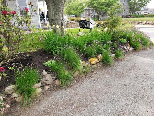 a garden with plants and a bench next to a street at Historic Block Island Suite in New Shoreham