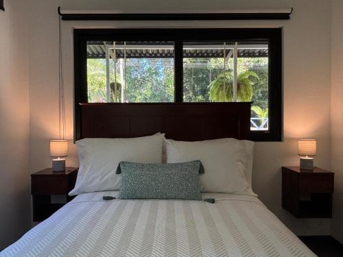 a bedroom with a bed with two lamps and a window at Luxury Riverfront House 3BR BBQ Jungle views & walk to river in Parrita