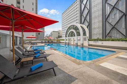 a swimming pool with lounge chairs and a red umbrella at BelAire Bangkok Sukhumvit in Bangkok