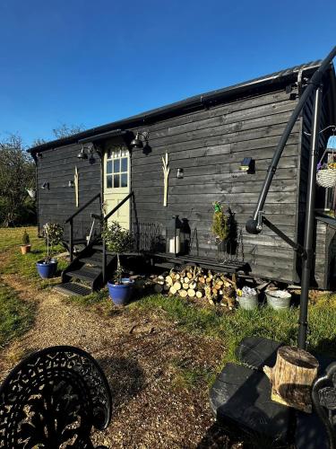 a black house with a fire pit in front of it at Mountbatten Shepherds hut & Buckhurst Shepherds hut in Ashford
