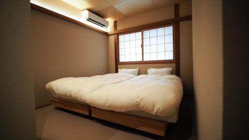 a bedroom with a white bed with a window at ゲストハウスとわ in Kanazawa