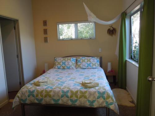 1 dormitorio con cama con edredón y ventana en Island Breeze, en Oneroa
