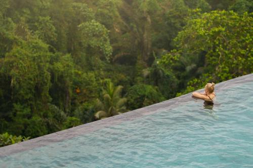 a woman in a swimming pool with a forest in the background at Kastara Resort in Ubud