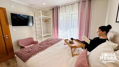 a woman sitting on a bed reading a book at Quinta de São José by PontaNegraAzores in Angra do Heroísmo