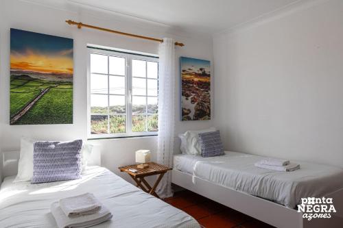 two beds in a white room with a window at Casa da Maresia by PontaNegraAzores in Biscoitos