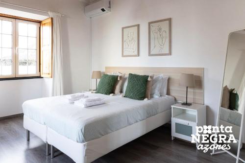 a white bedroom with a large white bed with green pillows at Casa da Gente by PontaNegraAzores in Biscoitos