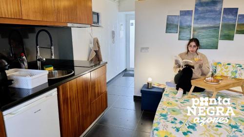 a woman sitting on a couch in a kitchen at Recanto das 5 by PontaNegraAzores in Cinco Ribeiras