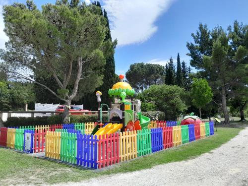 a playground with a colorful fence in a park at Camping Fontisson - Mobil home 3 pièces 4/5 personnes Climatisé MAE-1476 in Châteauneuf-de-Gadagne