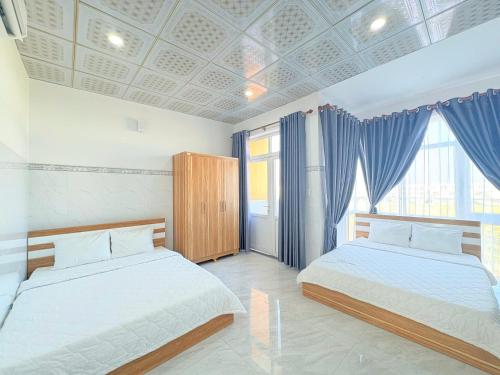 two beds in a bedroom with blue curtains at Homestay Đức Thạnh in Rạch Giá